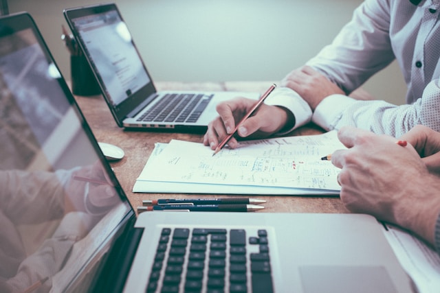 Two computers and two people discussing a real estate investment on paper